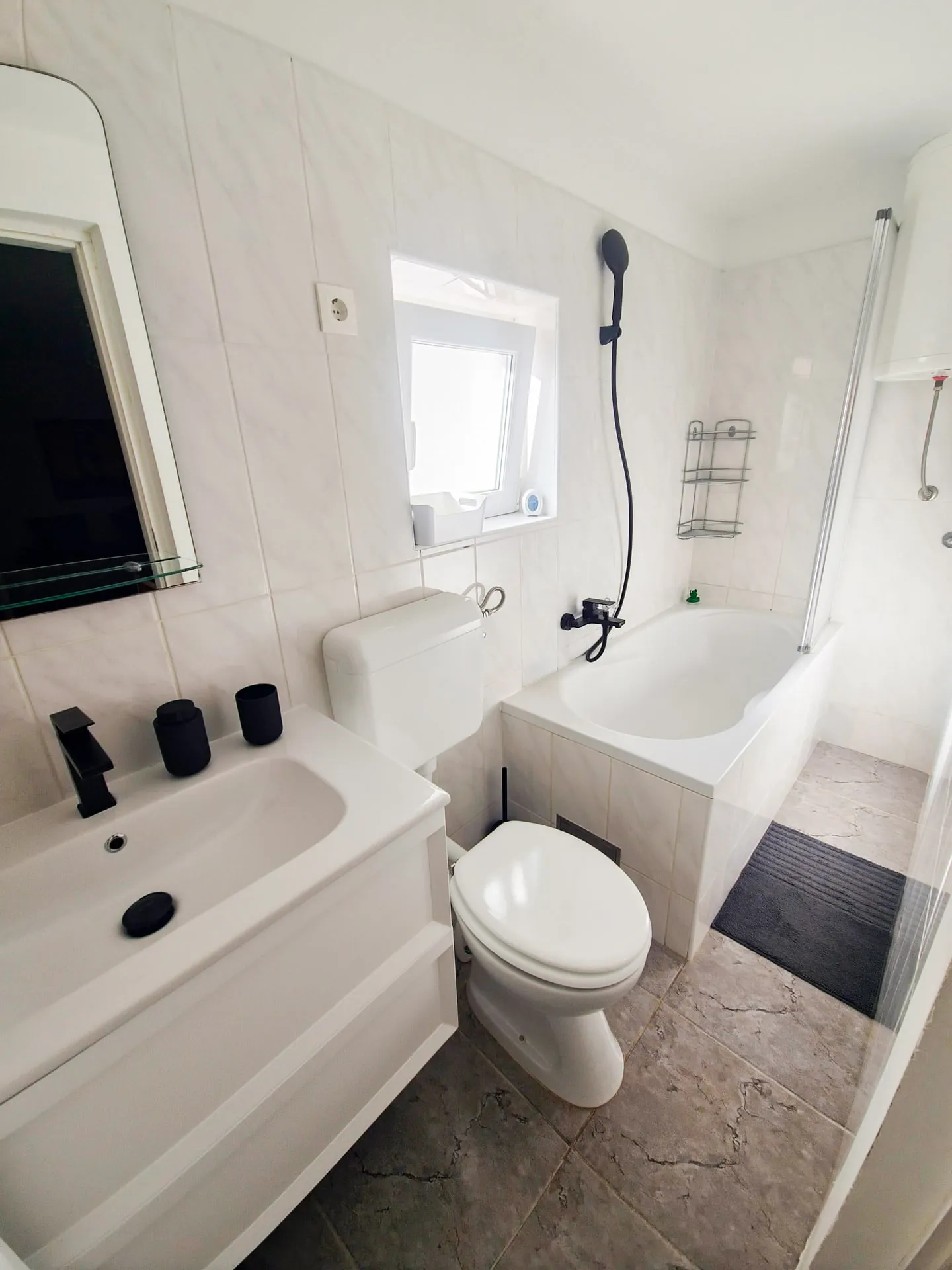 Bathroom with a white vanity unit, black tap and a bathtub with shower
